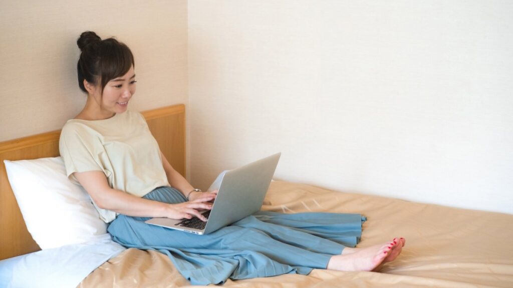 ベッドでくつろぐながらノートパソコンを使う女性